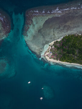 Aerial view of a tropical island in Guna Yala Comarca surrounded by turquoise coral reefs and deep blue Caribbean waters with small boats anchored in Guna Yala Comarca, Panama.