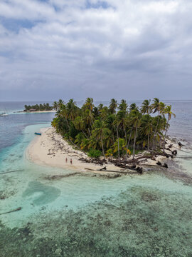 Aerial view of a tropical island in the San Blas archipelago with lush palm trees, white sand beach, and turquoise coral reef waters in Guna Yala Comarca, Panama.
