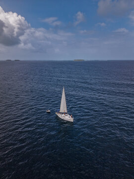 Aerial view of a white sailboat sailing on the deep blue Caribbean Sea with a small dinghy nearby under a cloudy sky in Guna Yala Comarca, Panama.