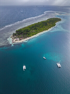 Aerial view of a lush tropical island surrounded by turquoise waters and coral reefs with sailboats anchored nearby in Guna Yala Comarca, Panama.