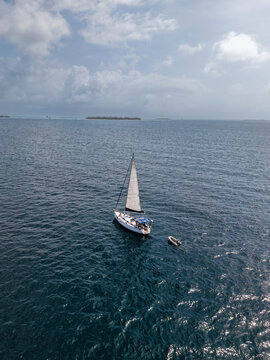 Aerial view of a sailboat and a small dinghy floating on the deep blue sea in Guna Yala Comarca, Panama.