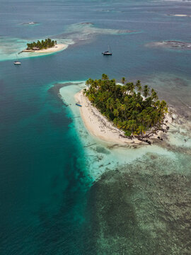 Aerial view of tropical islands surrounded by turquoise waters, coral reefs, and palm-fringed white sand beaches with sailboats anchored nearby in Guna Yala Comarca, Panama.