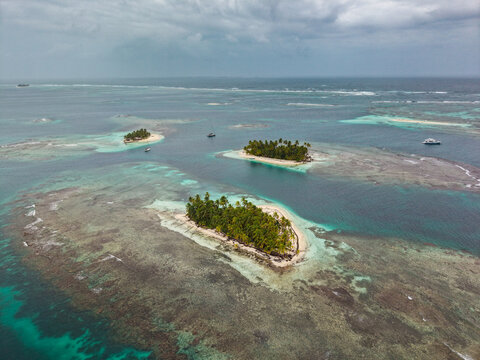 Aerial view of small tropical islands with lush palm trees surrounded by turquoise water and coral reefs, Guna Yala Comarca, Panama.