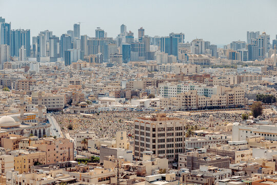 Aerial view of the dense urban landscape of Manama with modern skyscrapers rising above traditional buildings and a large cemetery in Manama, Capital Governorate, Bahrain.