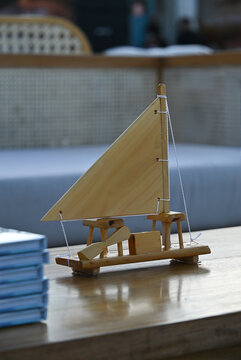 miniature wooden sailboat model on wooden table, handcrafted wooden jangada boat craft at seaside outdoor lounge, rustic nautical decor for tropical event close up