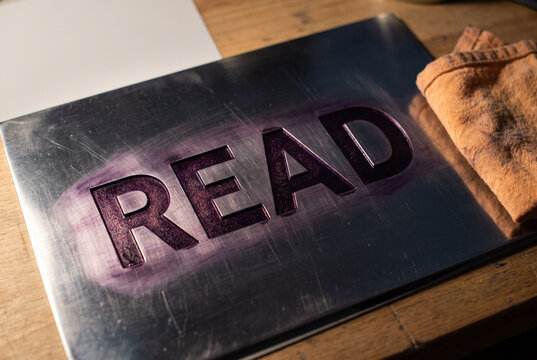 Read word in embossed metal sign with warm rustic workspace lighting