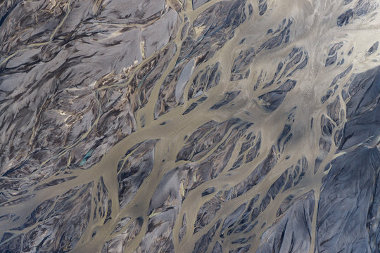 Aerial view of the braided river system near Mulakot, showing intricate glacial sediment patterns and winding water channels across the volcanic terrain, Rangarthing eystra, Iceland.