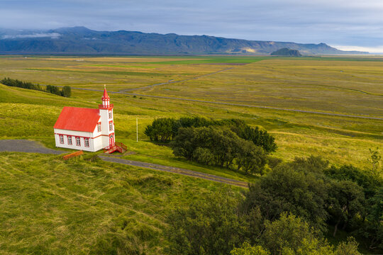 Aerial view of Mulakot church with its distinctive red roof and white walls, situated in the lush green landscape of Rangarthing eystra, Iceland.
