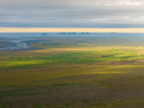 Aerial view of the vast green landscape near Mulakot with distant islands on the horizon under a dramatic cloudy sky in Rangarthing eystra, Iceland.