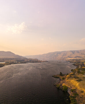 Aerial view of the Columbia River flowing through a landscape affected by wildfire smoke and haze, with rolling hills and dry vegetation in The Dalles, Oregon, United States.