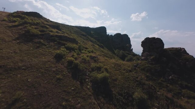 Dynamic low altitude FPV drone footage gliding over grassy mountain slopes and rocky cliffs at Babin Zub peak on Stara Planina, Serbia. Cinematic aerial view of alpine landscape, ski lift infrastructu