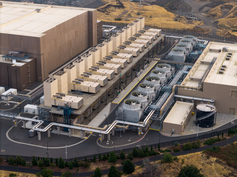 Aerial view of the Google Data Center featuring rows of cooling towers and industrial piping set against a dry landscape under hazy conditions in The Dalles, Oregon, United States.