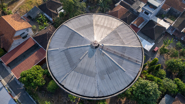 Aerial view of a circular water tower with a corrugated metal roof and a ladder, surrounded by residential houses and trees in Klaten, Central Java, Indonesia.