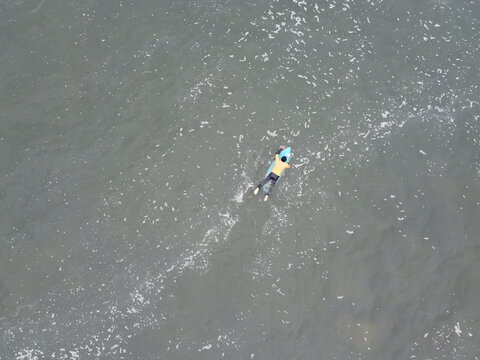 View of a surfer in a yellow shirt paddling on a blue surfboard in the ocean at Playa Punta Hermosa, Punta Hermosa, Lima Province, Peru.