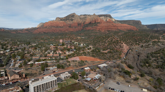 Sedona, Arizona, United States - 30 December 2023: Aerial view of red rock formations towering over the town of Sedona with desert vegetation and buildings under a clear sky.
