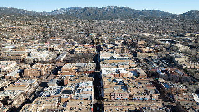 Santa Fe, United States - 30 December 2023: Aerial view of the Santa Fe skyline featuring adobe-style architecture, historic buildings, and distant snow-capped mountains under a clear sky.