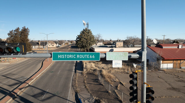 Tucumcari, United States - 26 December 2023: Aerial view of the historic Route 66 sign overlooking a quiet street with traffic lights and nearby buildings under a clear blue sky.