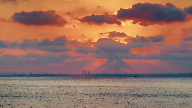 Dramatic clouds glow with pastel sunset hues as sunbeams break through sky above Istanbul skyline over Marmara Sea. Timelapse