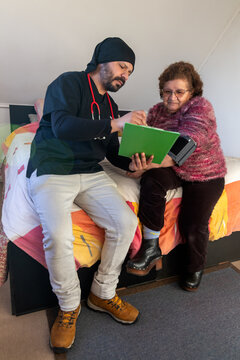 A male home health care provider gives instructions to his elderly female patient in her bedroom at home