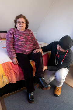 A man home health care provider examines an elderly Latina woman in the bedroom of her home
