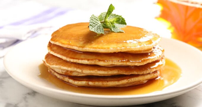 Man adding mint to pancakes with maple syrup at white marble table, closeup