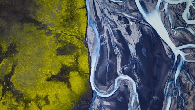 Aerial view of the braided river channels of Tungnaa flowing through dark volcanic sand alongside vibrant green mossy terrain in Skaftarhreppur, Iceland.
