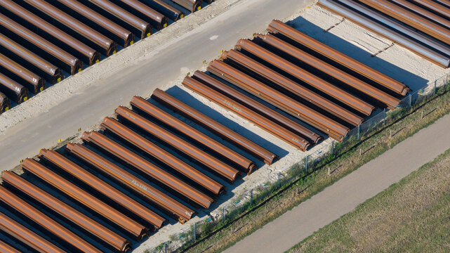 Aerial view of rows of long brown curved metal sheet piles stored in an industrial yard in Ochten, Gelderland, Netherlands.