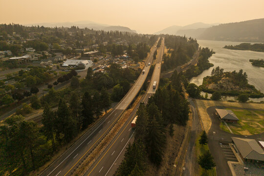 Aerial view of Interstate 84 winding through Hood River with hazy wildfire smoke filling the air above the Columbia River and highway traffic in Hood River, Oregon, United States.