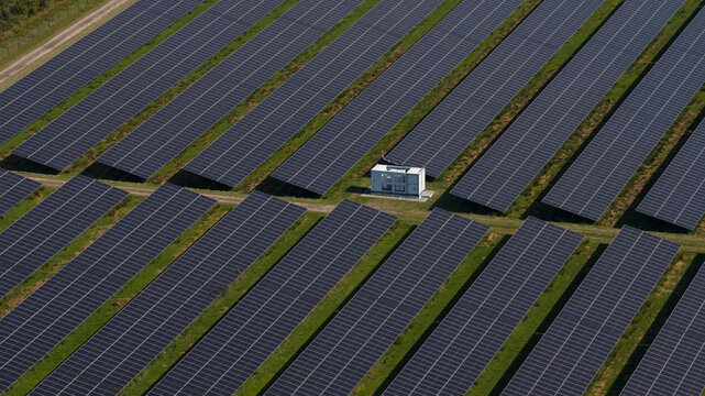Aerial view of a large solar farm with rows of photovoltaic panels and a central transformer station in Oude Pekela, Groningen, Netherlands.