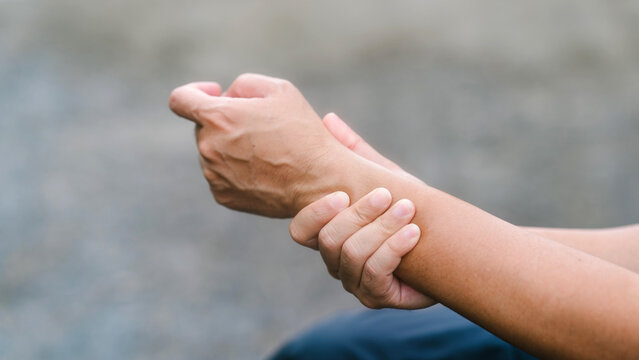 Side view of a person clutching a painful wrist and experiencing hand numbness. Demonstrating peripheral neuropathy, nerve compression, chronic gout, physical exhaustion, and unwellness.
