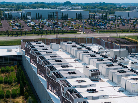 Aerial view of Hillsboro data centers featuring rows of industrial HVAC cooling units on a flat roof with a large parking lot in Hillsboro, Oregon, United States.