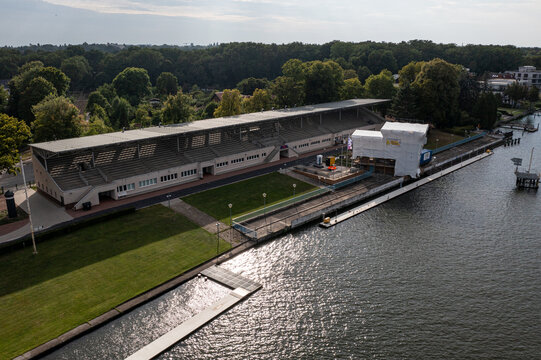 Aerial view of the historic Regattatribune Berlin-Grunau grandstand situated along the riverbank with lush green lawns and construction work in Berlin, Berlin, Germany.