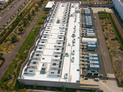 Aerial view of the Hillsboro data center complex featuring rows of cooling units on the white roof, adjacent parking areas, and surrounding landscape in Hillsboro, Oregon, United States.