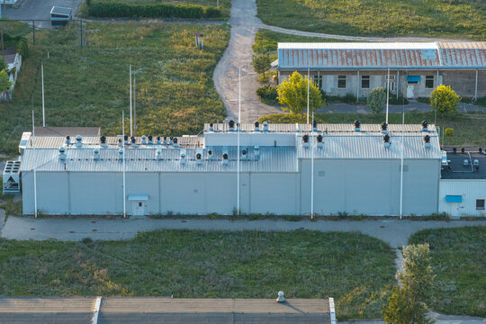 Aerial view of a pharmaceutical laboratory facility featuring multiple external chillers on the roof and tall lightning protection rods, situated in an industrial area in Poland.