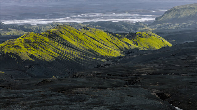 Aerial view of vibrant green moss-covered mountains contrasting with dark volcanic lava fields in the Icelandic highlands, Skaftarhreppur, Iceland.