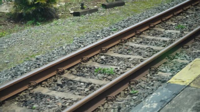 Weathered railway tracks with gravel ballast stretch through greenery and station platform. Industrial transport infrastructure detail shot for commercial use, elegantly showcasing train.