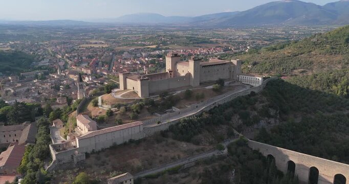Aerial view of the historic Rocca Albornoziana fortress overlooking the city of Spoleto with its stone walls and towers set against the rolling hills of Umbria, Spoleto, Umbria, Italy.