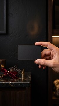 Person holding a blank black card in front of a dark interior background