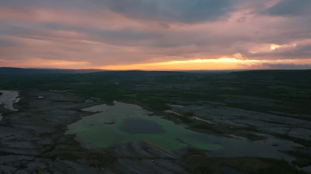 Aerial view of sunset over limestone karst landscape with green water pools in Burren Ireland.