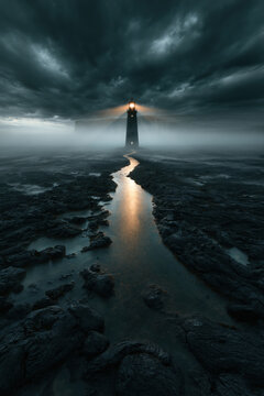 Lighthouse storm fog water sea coast rock path light dark landscape with solitary lighthouse in storm fog over flooded coast and rocky shore, dramatic sky, moody seascape