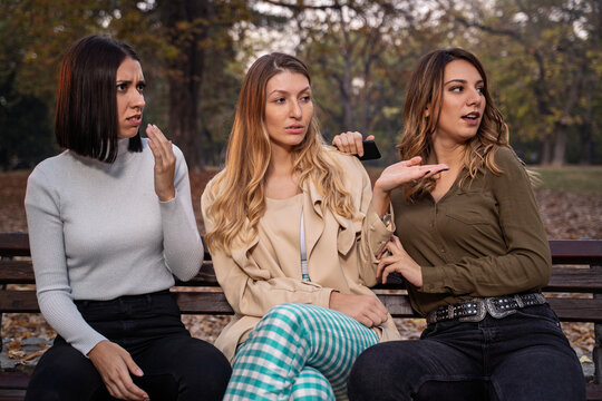 Three young girls on park bench gossiping or shocked by the situation 