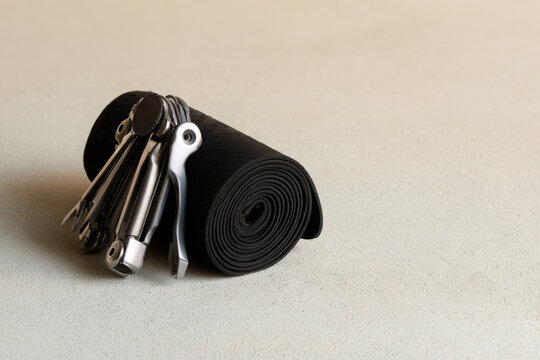 Compact bicycle repair multitool beside a rolled black inner tube on a neutral surface, representing cycling maintenance, roadside repair and practical bike equipment.