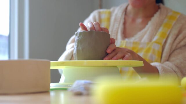 Closeup woman hand builds a textured clay cup on a yellow turntable, capturing the creative joy of ceramic crafting