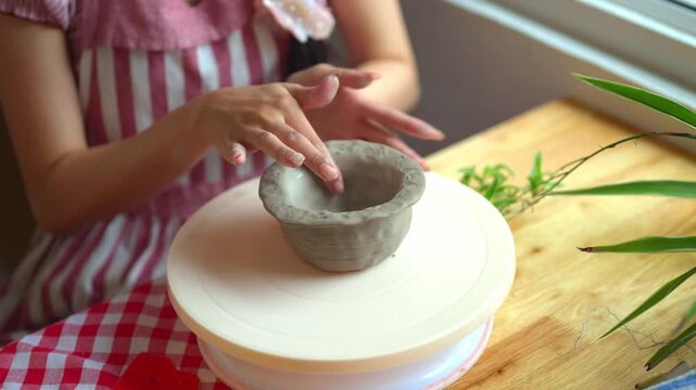 Woman Shaping Clay Bowl by Hand on Pottery Turntable at Wooden Table Indoors