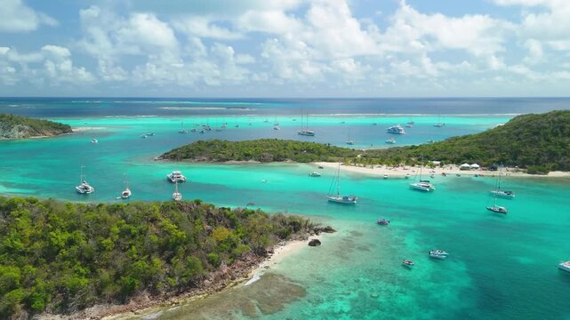 Aerial parallax weaves through the channel between Petit Rameau and Baradal as dozens of yachts anchor across Tobago Cays' turquoise reef flats