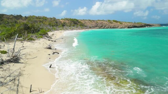 Aerial flight skims along the empty white sand of Petit Carenage Beach in Carriacou, Grenada beside turquoise water and a driftwood strewn shore
