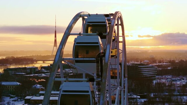 Drone slides left past a Ferris wheel with Riga skyline glowing at winter sunset