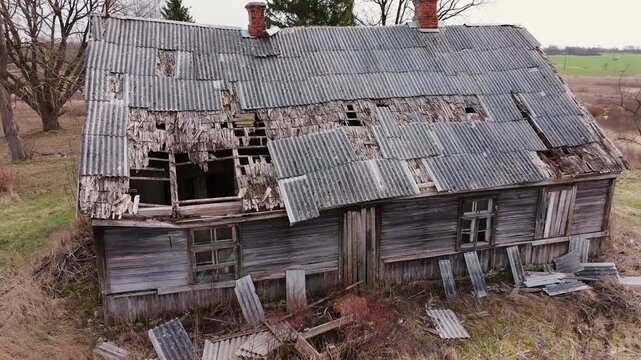 Drone turns left, abandoned wooden home revealing broken roof and decay outside