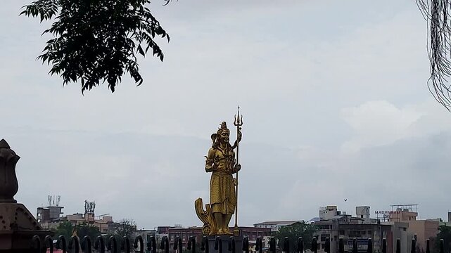 Golden Shiva statue at Sursagar Lake, Vadodara, Gujarat, India, zooming toward iconic Hindu landmark surrounded by urban cityscape and water.