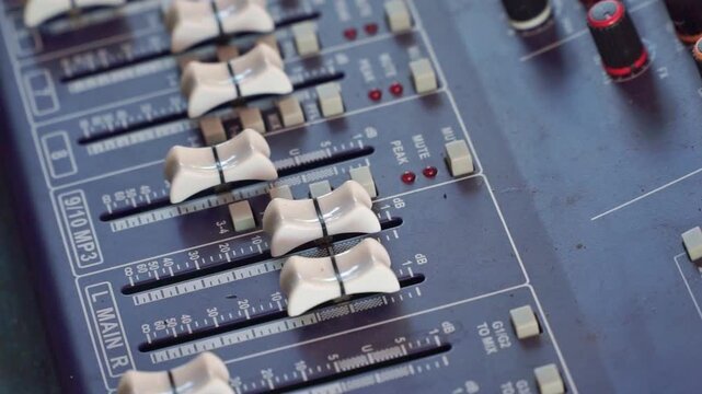 Hand operating professional audio mixer close up, colorful knobs and faders, sound engineering and studio concept.